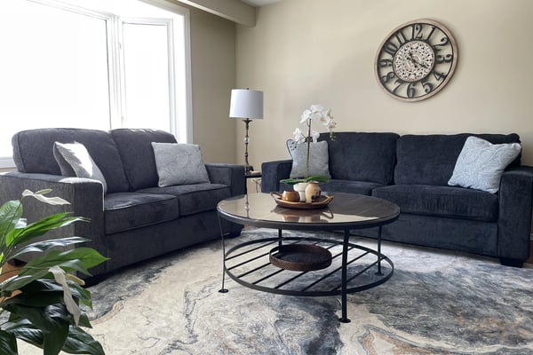 Living room with dark sofas, marble-patterned rug, and decorative wall clock at Hammer Haus III
