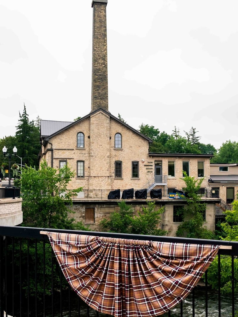 Old mill building with tall chimney and tartan bunting over the Grand River, Fergus